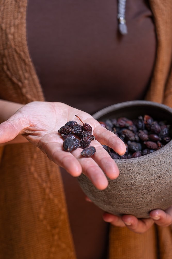 Mani che mostrano alcune bacche essiccate sul palmo, sopra una ciotola rustica