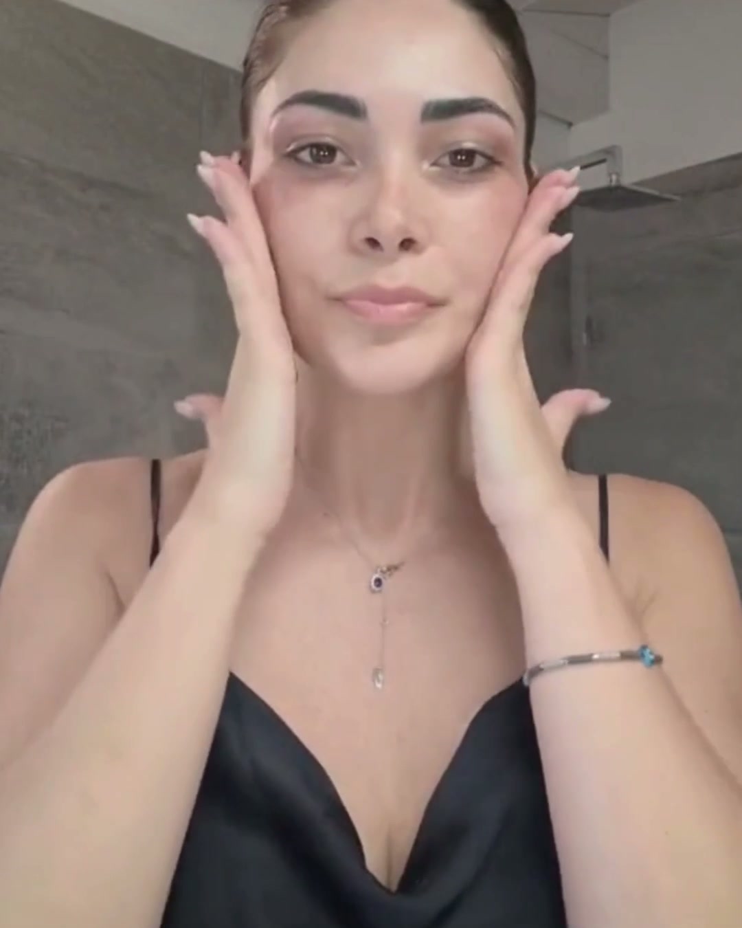 Una donna frontale, con le mani posate sulle guance, in un bagno moderno dalle pareti di pietra